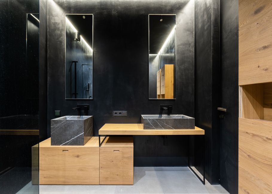 Washbasins with faucets placed on wooden table and cabinet near black wall with mirrors in modern washroom with door at home
