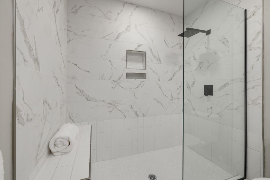 Elegant white marble shower with glass door, bench, and towel in modern bathroom.