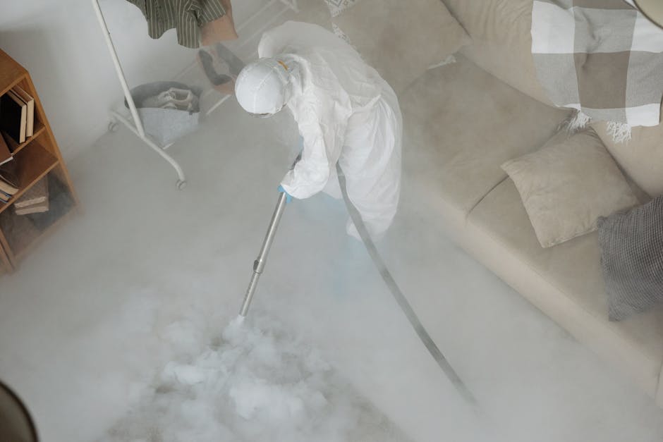 A person in protective gear disinfects a living room using a fogging machine for sanitation.