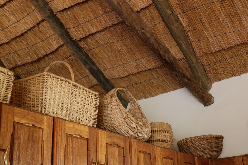 Cozy kitchen interior with a straw roof, wooden cabinets, and wicker baskets on display.