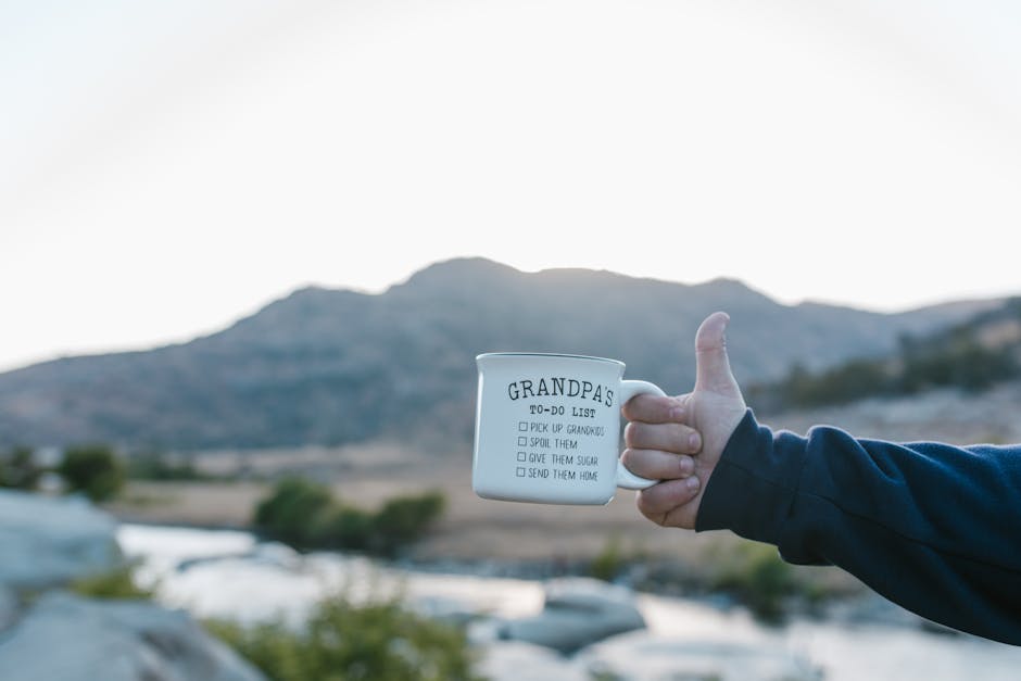 Outdoor close-up of a ceramic mug with text held up against a scenic mountain backdrop.
