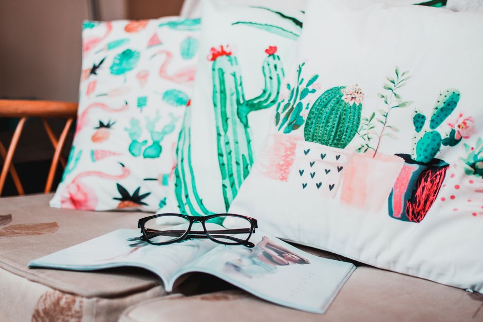 Stylish indoor living area featuring cactus-themed cushions and reading glasses on a sofa.