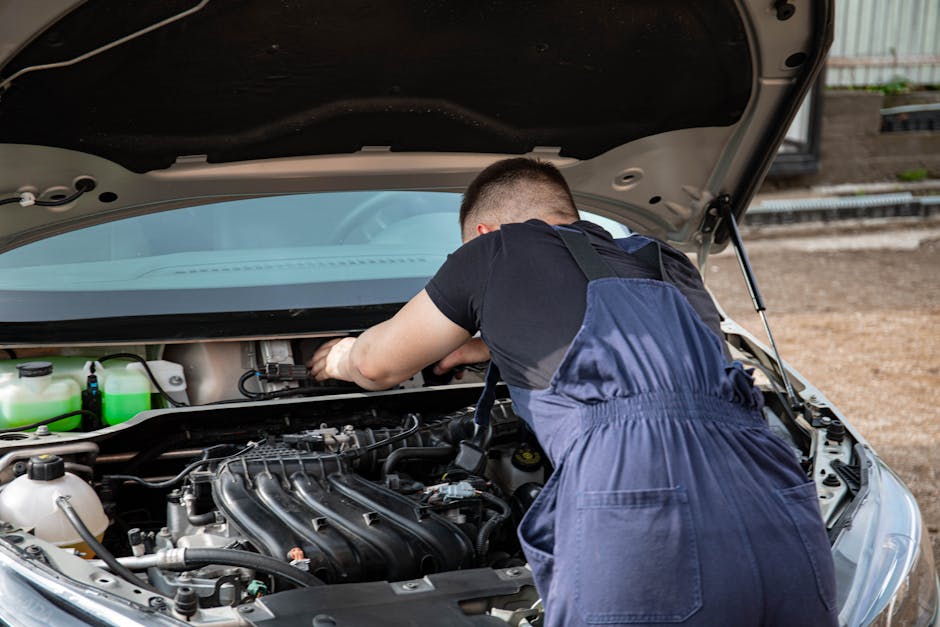 Back view of a mechanic fixing a car engine outdoors during the day.