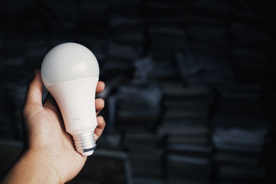 Crop unrecognizable person reaching out hand with light bulb against heap of books in dark room